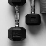 Dois halteres e colchonete de exercícios vistos de cima, ilustrando treino de força e suplementação