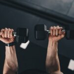 Praticante realizando exercício com halteres na academia