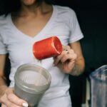 Pessoa despejando proteína em pó em recipiente para preparar bebida, foto ilustrativa de whey protein