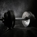 Halter em ambiente de musculação representando treino de força e uso opcional de luvas